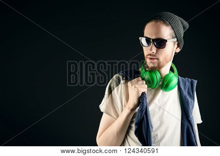 Trendy young man in hat and sunglasses posing over black background. Youth style.