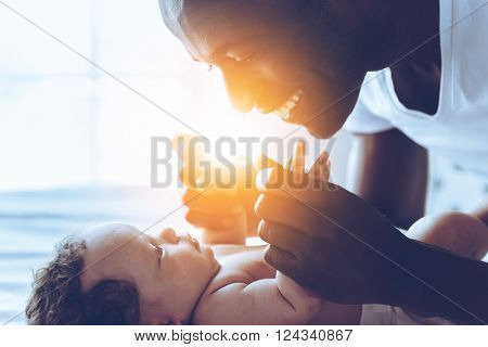 You are my everything! Side view of happy young African man playing with his little baby and smiling while lying in bed