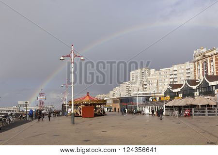 Scheveningen, Netherlands, 27 march 2016: people walk under grey sky and rainbow on scheveningen boulevard in holland