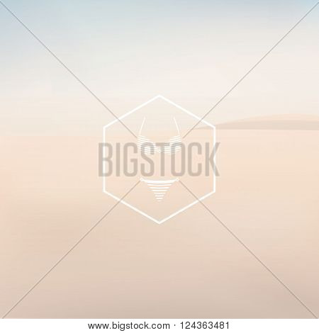 Bikini sexy fashion symbol in hexagon badge. Sandy beach in haze landscape vector background. Eps10 vector illustration.