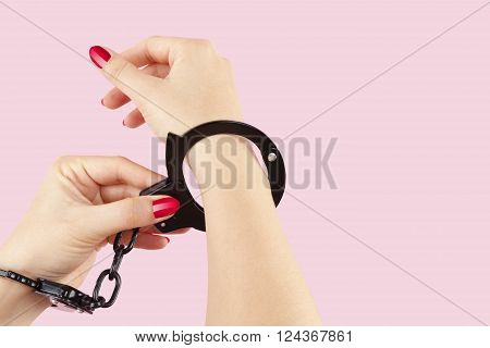 Female hands in black handcuffs isolated on pink background. Ilegal concept.