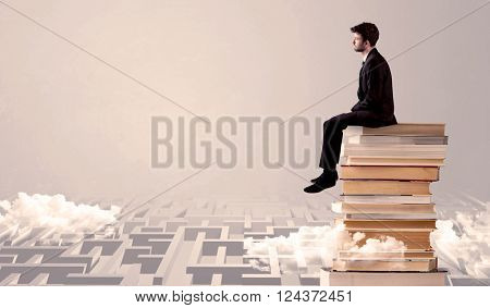 A serious businessman in suit sitting on a pile of giant books in front of a grey wall with clouds, labirynth