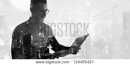 Double exposure bearded businessman wearing black shirt and glasses.Banker holding contemporary notebook hands, work online banking. Modern skyscraper city background.