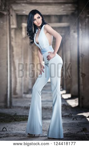 Portrait of beautiful sexy young woman with elegant overall, in urban background. Attractive young brunette with long hair and blue eyes posing fashion in white outfit. Long legs woman, side view