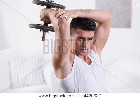 Fit young man strengthening arm muscles with dumbbell