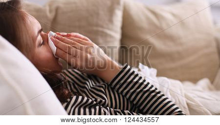 Portrait of a sick woman blowing her nose while sitting on the sofa.