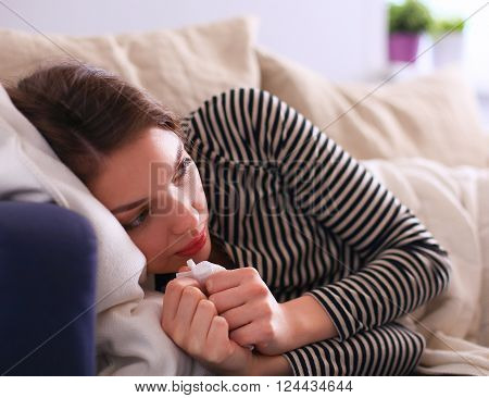 Portrait of a sick woman blowing her nose while sitting on the sofa.
