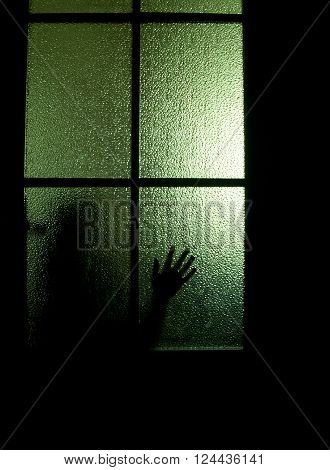 Blurred silhouette of a child behind a glass door in the darkness (symbolizing sadness loneliness horror or fear)