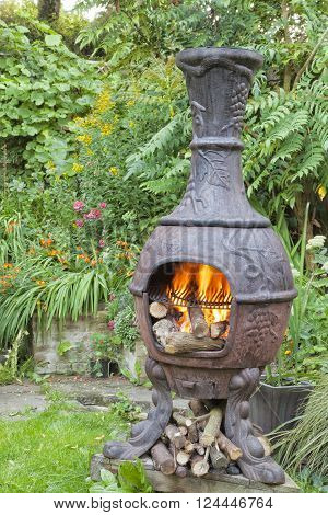 Rustic cast iron wood burning stove Mexican chiminea with flames ready for barbeque in summer cottage flower garden