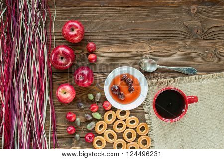 red cup of tea ripe red apples actinidia berries bagels strawberry jam in white saucer spoon red napkin at white polka dots on wooden table with decorative colorful dry straw. top view