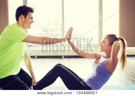 fitness, sport, training, teamwork and people concept - happy woman with personal trainer doing sit ups and high five gesture in gym