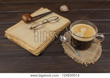 Old books, eyewear and cup of coffee on a dark wooden table. Reading vintage old book and coffee. Relax with a book and a good coffee.
