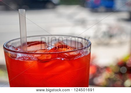 Red cordial drink in a cup, with ice and straw.