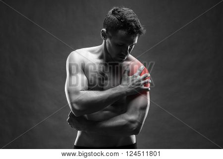 Pain in the shoulder. Muscular male body. Handsome bodybuilder posing on gray background. Black and white photo with red dot
