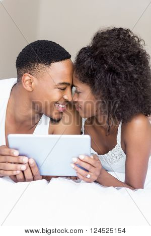 Young couple cuddling each other while holding digital tablet in bedroom