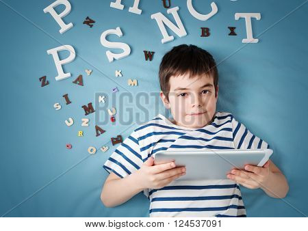 seven years old child lying with tablet and letters on blue background