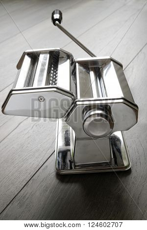 Metal reflective pasta machine with add-on and hand crank wood surface. Selective focus on middle of pasta machine. Concept of food preparation.
** Note: Visible grain at 100%, best at smaller sizes