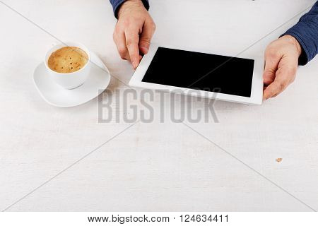 Man holding tablet while sitting at the white rustic wooden table. Man communicates using tablet computer