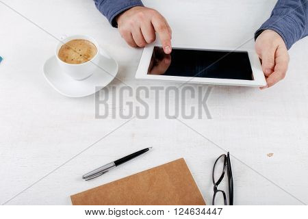 Man clicks on screen tablet computer while sitting at the white rustic wooden table. Man working using tablet computer
