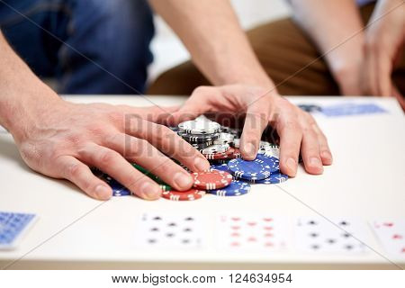 leisure, games, gambling and entertainment - close up of male hands with casino chips and playing cards making bet or taking win at home