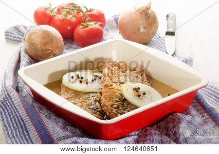 fried herringfilet with onion pepper and mustard seeds in a bowl fresh tomato and kitchenknife in the background