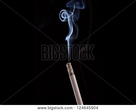 Burning cigarette with smoke on black background