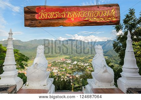 Back view of white lion statue at Wat Phra That Doi Kong Mu with aerial city view of Mae Hong Son against the mountain ranges, Thailand.
