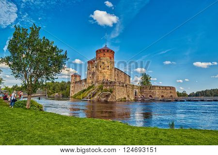 Lake view with grass and reflections of Olavinlinna Olofsborg, the 15th-century medieval three-tower castle located in Savonlinna, Finland.
