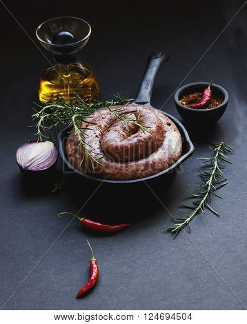 raw beef sausages on a cast-iron pan with rosemary and spices on a wooden table South African boerewors