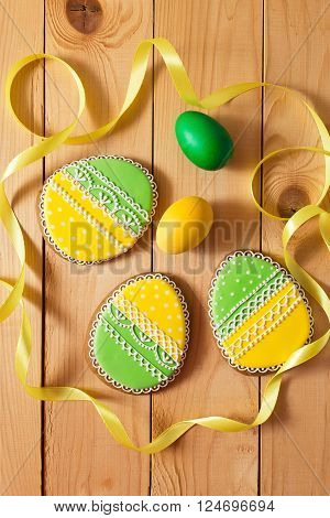 Easter homemade gingerbread cookie and yellow end green eggs with ribbon over wooden table. Colorful image top view