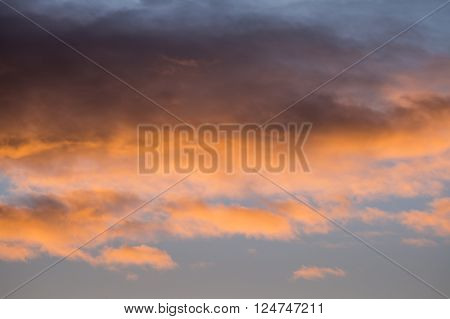 Rain clouds colored pink on a blue background by the sun during sunrise or sunset.