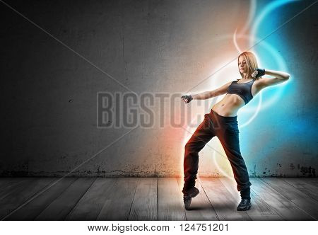 Girl dancer stands leaning back with lifted up left hand bent at the elbow. Glowing light lines are following her move on dark background.