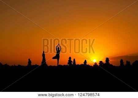 Summer sunset yoga session on beautiful Playa del Duque beach with stone pile stacks silhouettes - tropical Tenerife island, Canary in Spain. Vriksha-asana, tree pose