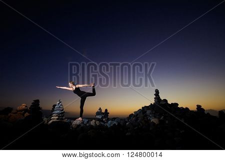 Summer sunset yoga session on beautiful Playa del Duque beach with stone pile stacks silhouettes - tropical Tenerife island, Canary in Spain. Warrior pose - Virabhadrasana