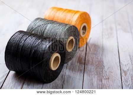 black gray orange waxed thread for hand-stitching leather on a wooden background