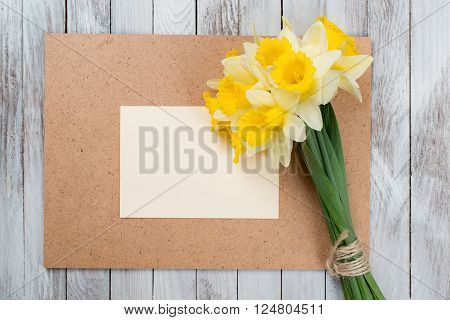 Fresh spring yellow daffodils flowers and empty tag on a brown painted wooden planks. Selective focus. Place for text.