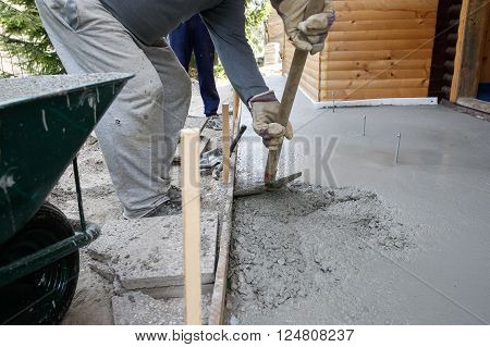 Masons filling wood form with a shovel of concrete mix for floor base in front of the house. Construction business and tools do-it-yourself basic work around the house concept.