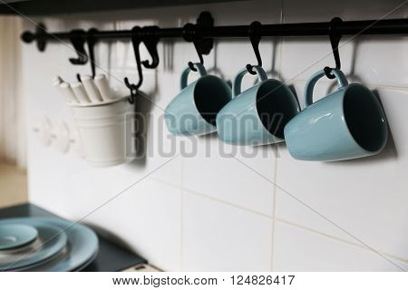 Blue cups is located on the pure white wall in the kitchen above the owen. closed to cups are located some other applience needed for cooking
** Note: Shallow depth of field