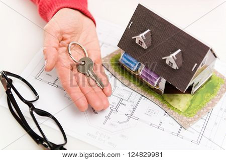 Closeup of woman hand giving residential house key to client. Concept of housing rent and sale. Shallow depth of field.