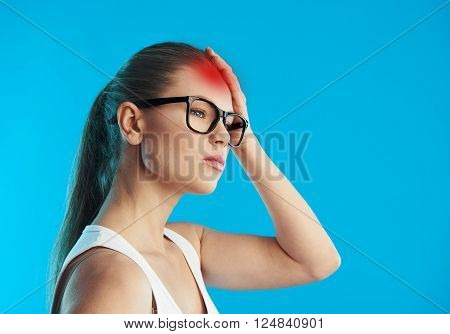 Portrait of young sick female suffering from migraine or vertigo over blue background. Concept of head illness diagnosis and treatment.