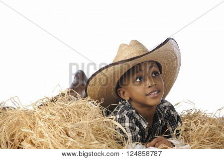An African cowboy happily resting in the hay cowboy boots and an over-sized hat.  On a white background.