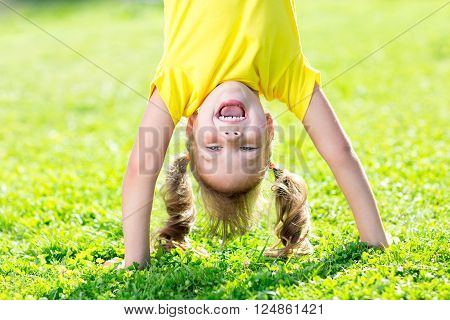 happy kid girl standing upside down on her head on grass in summerday