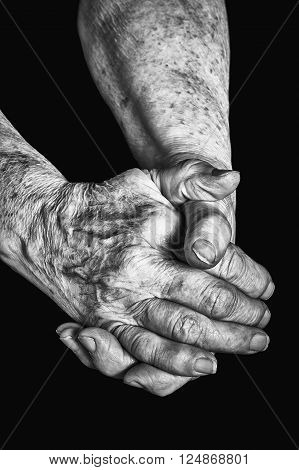Old woman clasps her hands on a black background
