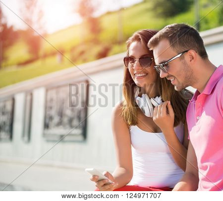 Young smiling couple in summer street using smartphone