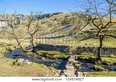 Low bridge over Malham Beck near Malham Cove in attractive landscape with footpath and gate in the stone wall.