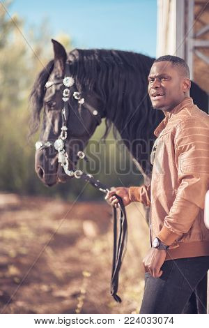 african Man wearing sunglasses near a black horse in hangar