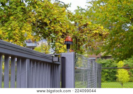 Steel gate with flashing light and steel fence and trees and park in the background