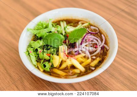 Laksa on wooden table. Laksa is a spicy noodle soup popular in the Peranakan cuisine.