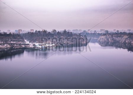 Fantastic purple landscape of the lake and the little workers buildings in the quarry, homes of the big city in the background