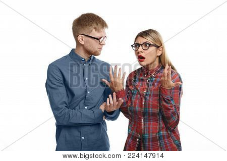 Stylish young European couple in glasses having arguement in studio: emotional blonde girl with fed up look, feeling tired and stressed while explaining her grumpy bearded husband thar she is right